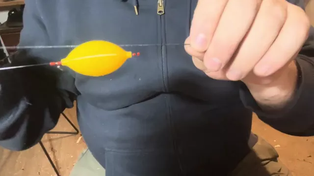 Mano sosteniendo la línea con una boya aceituna amarilla, sobre un buzo azul